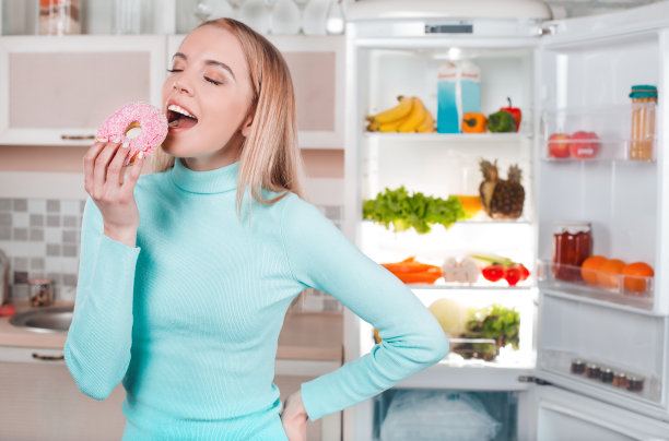 年轻的金发女郎在家冰箱旁边图片下载