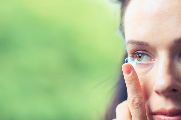 一个女人把隐形眼镜放进眼睛的特写。素材图片