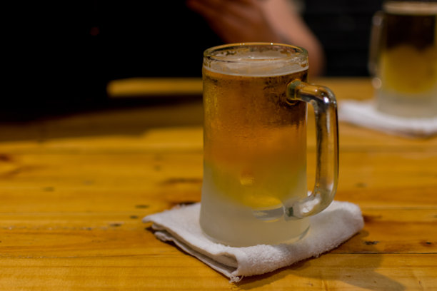 啤酒杯里的啤酒加冰和泡沫放在一张木桌上图片下载