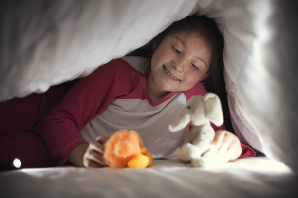 女孩躲在被子里用手电筒玩玩具图片下载