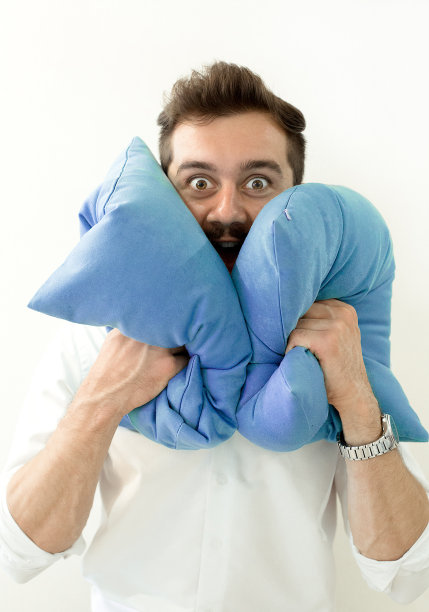 男人需要沉默。伤心疲惫的年轻男子用枕头闭上耳朵，保护自己免受噪音的伤害，有头痛的感觉。他不想听或者睡不着。失眠问题的概念。男人拥抱枕头图片下载