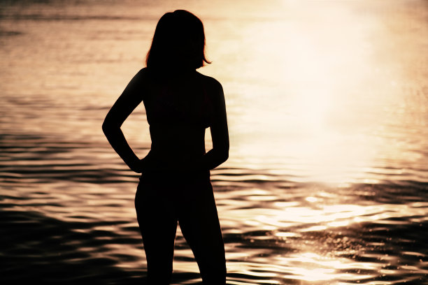 海上日落的女人。比基尼女人的剪影背光图片下载