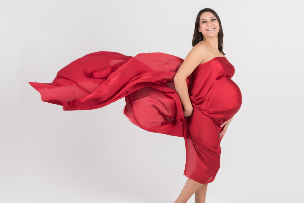 美丽优雅的孕妇摆姿势与红色缎子布图片下载