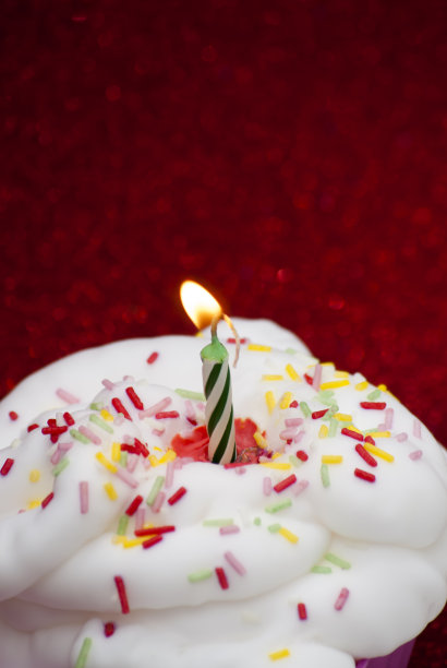 鲜红色背景上点燃蜡烛的纸杯蛋糕图片下载