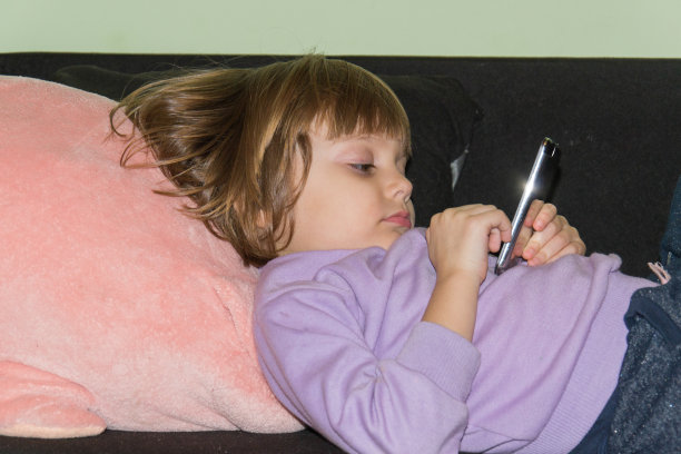 可爱的小女孩躺在床上和她的毛绒玩具猪和手机图片下载