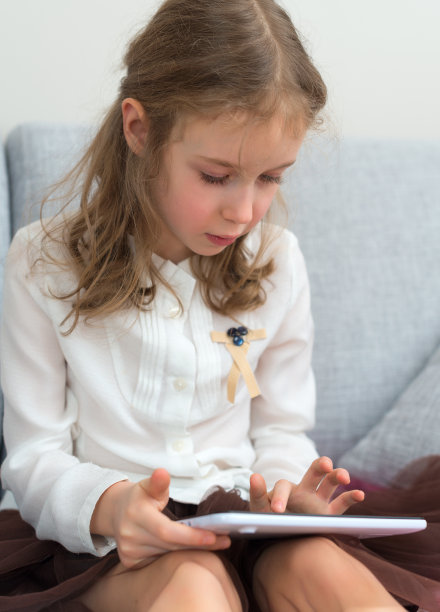 小女孩坐在沙发上使用平板电脑。图片下载