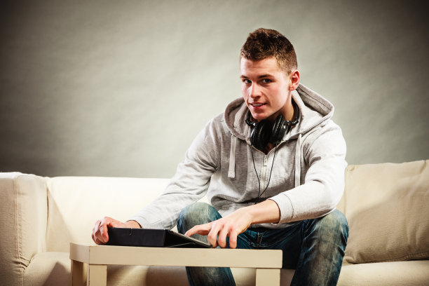 年轻人戴着平板电脑耳机坐在沙发上图片下载