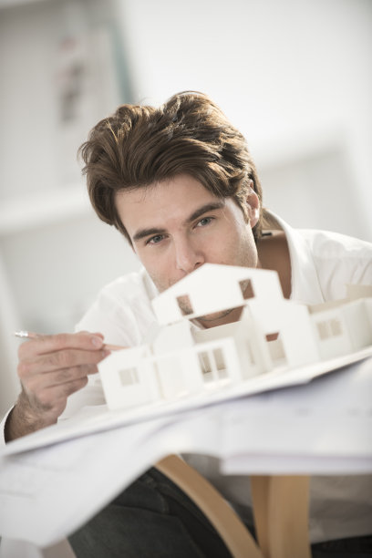 一个人正在研究建筑项目和一个模型房子图片下载