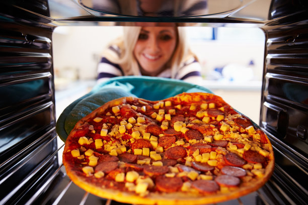 一个女人把意大利辣香肠披萨放进烤箱煮图片下载