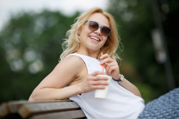 戴着墨镜的金发女孩坐在公园的长椅上笑着图片下载