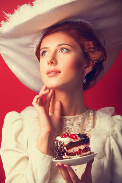 红发爱德华王朝妇女的肖像与蛋糕在红色的背景。图片下载