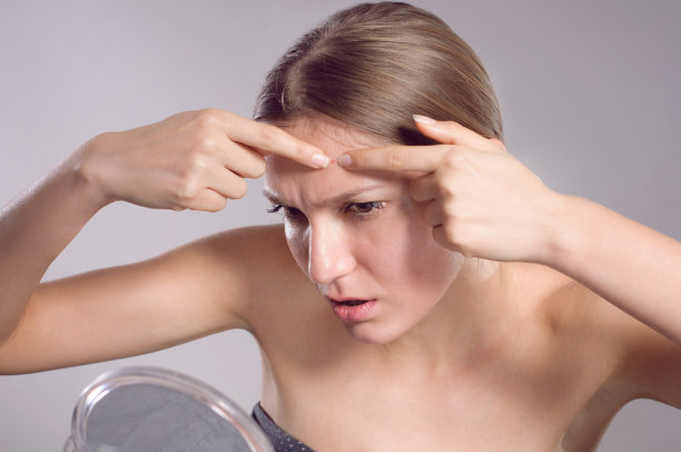 一个年轻女子在镜子前捏捏脸上的粉刺图片下载