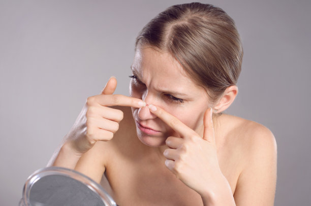 一个年轻女子在镜子前捏捏脸上的粉刺图片下载