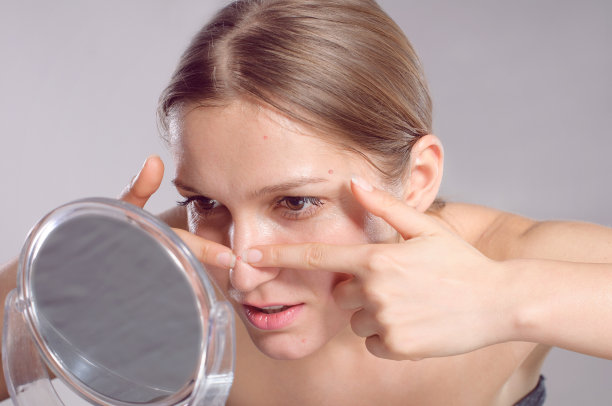 一个年轻女子在镜子前捏捏脸上的粉刺图片下载