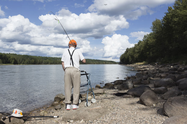 一位老人肩上扛着钓竿沿着海岸散步图片下载