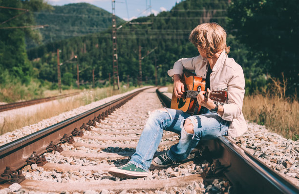 一个拿着吉他的年轻人坐在铁路上图片下载
