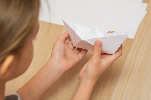 一个女孩看着一只手工做的纸船图片下载