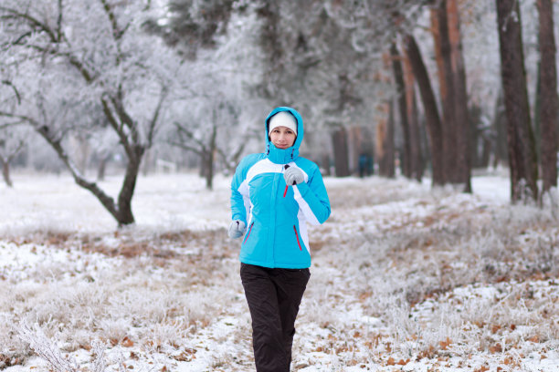 微笑的年轻女子在冬季公园慢跑。图片下载