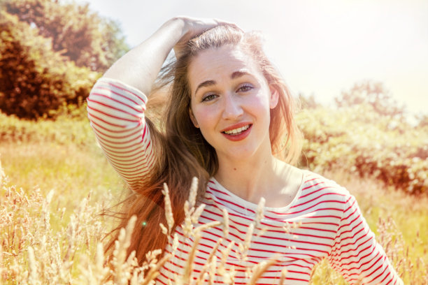 在阳光明媚的乡村，美丽的年轻女子挽着头发微笑着图片下载