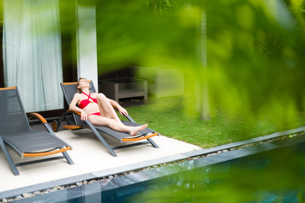 在游泳池附近的躺椅上休息的女人。图片下载