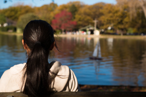 年轻女子在湖上看模型游艇图片下载