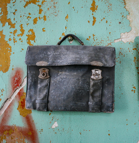 破旧的黑色公文包，背景是一堵裂墙图片下载