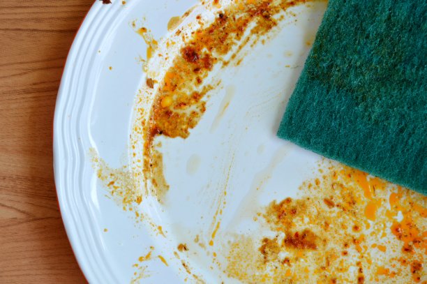 绿色擦洗海绵清洁白色盘子上的食物污渍图片下载