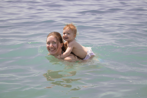妈妈背着小女孩。幸福的家庭游泳图片下载