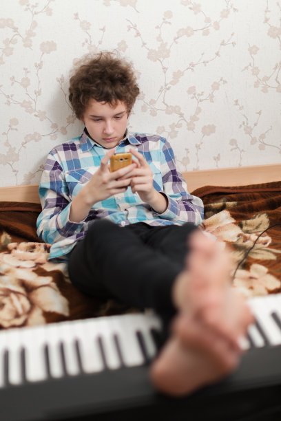 男孩把脚放在钢琴上玩手机图片下载