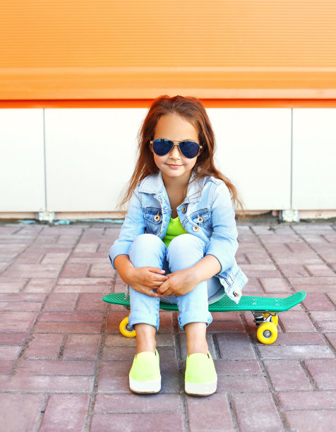 美丽的小女孩坐在滑板上在城市素材图片