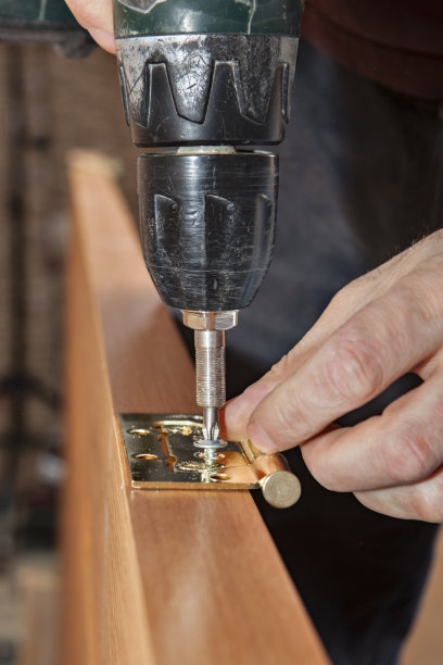 使用螺丝刀枪紧固门铰链的细木工螺钉。图片下载