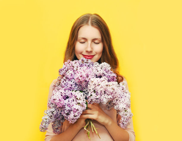 快乐微笑的女人享受着淡紫色的花香越过黄色素材图片