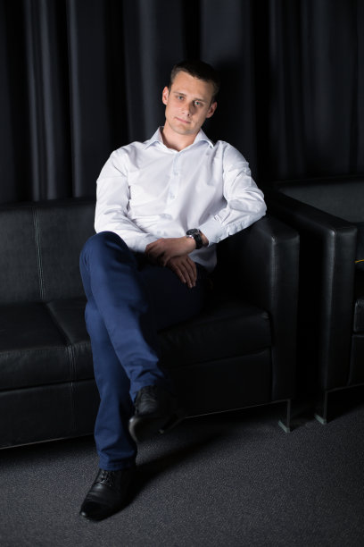 在黑暗的背景上，一个年轻人在扶手椅上摆姿势图片下载