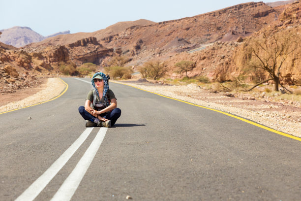 年轻女子坐在沙漠柏油路上。图片下载