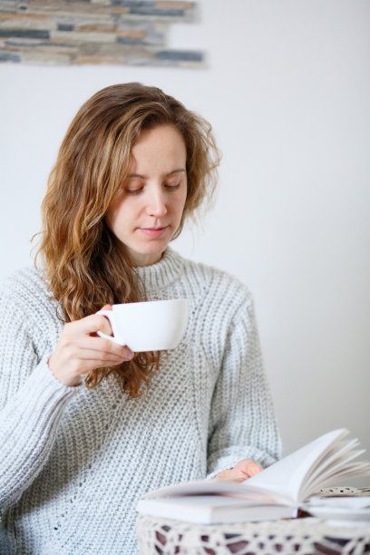 女人一边看书，一边拿着盛有咖啡或茶的杯子图片下载