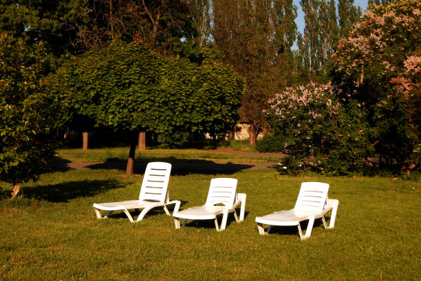 茅屋前的绿草坪上放着塑料躺椅图片下载