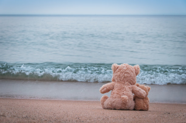 泰迪熊坐在美丽的海滩上。图片下载