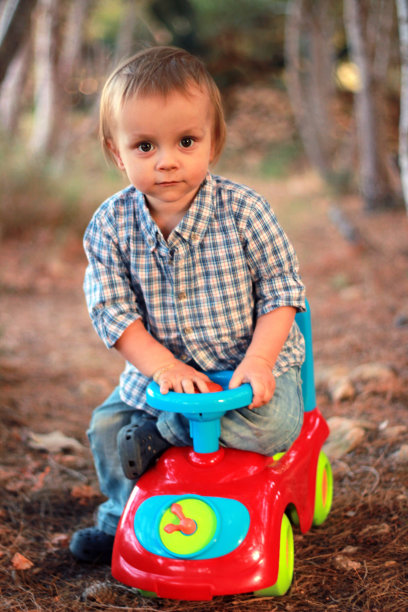 一个小男孩坐在公园里的玩具车上图片下载