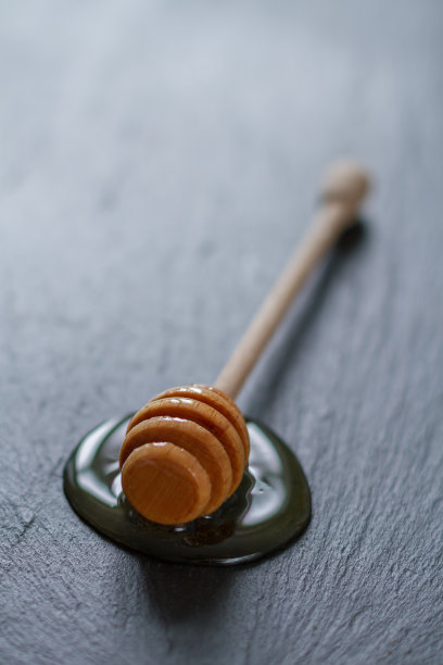 蜂蜜勺与蜂蜜溢出在黑色的石头背景图片下载