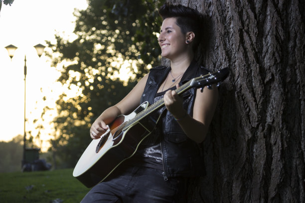 弹吉他的少女，快乐。靠在树上。图片下载