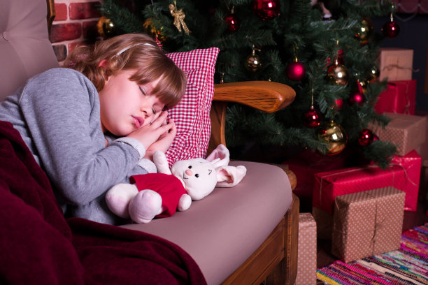 女孩睡在圣诞树旁的沙发上，旁边放着礼物图片下载