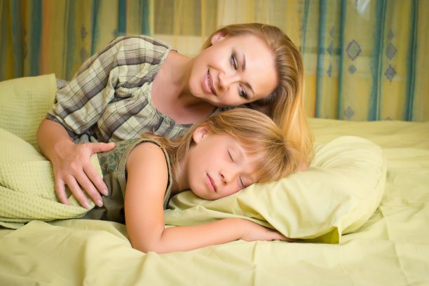 美丽的母亲微笑着拥抱她在床上睡觉的可爱的女儿。图片下载