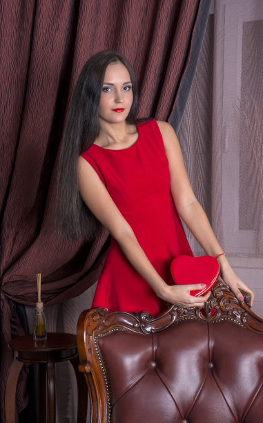 年轻女子坐在皮椅上，手捧红心图片下载