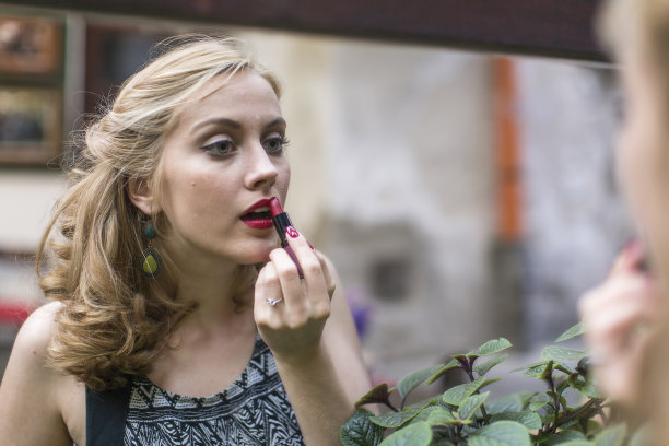 在镜子旁边涂口红的漂亮年轻女人。图片下载