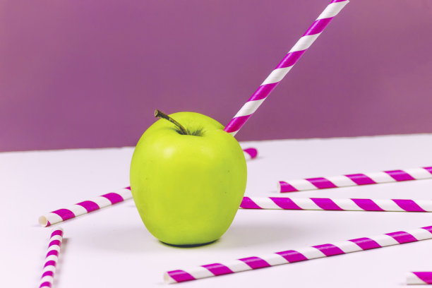 绿色苹果与条纹稻草在紫色的背景图片下载