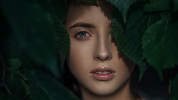 特写有吸引力的年轻女人。透过树叶看的脸。图片下载