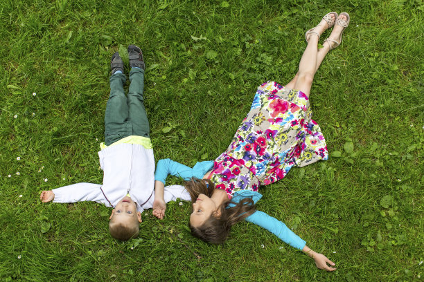 可爱的女孩和她的小弟弟躺在绿色的草地上。图片下载