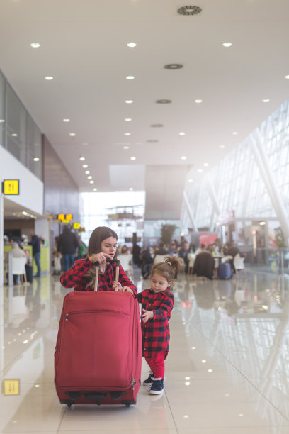 妈妈和可爱的蹒跚学步的女孩一起拉着一个手提箱图片下载