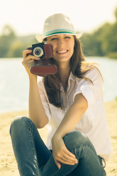 年轻时髦的女孩拿着旧胶卷相机在海滩上。图片下载