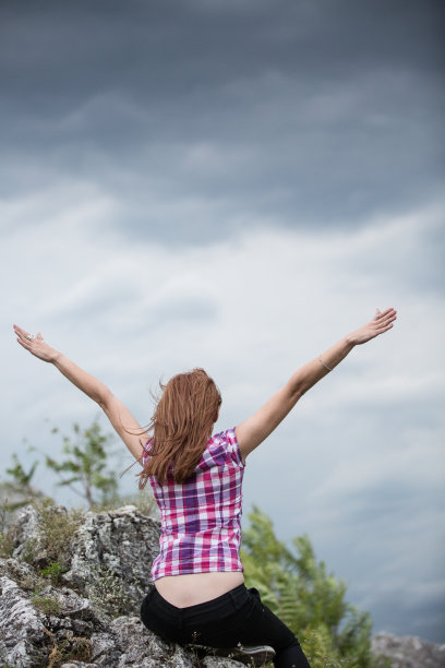 女孩在有风的夏天在高高的岩石上享受图片下载